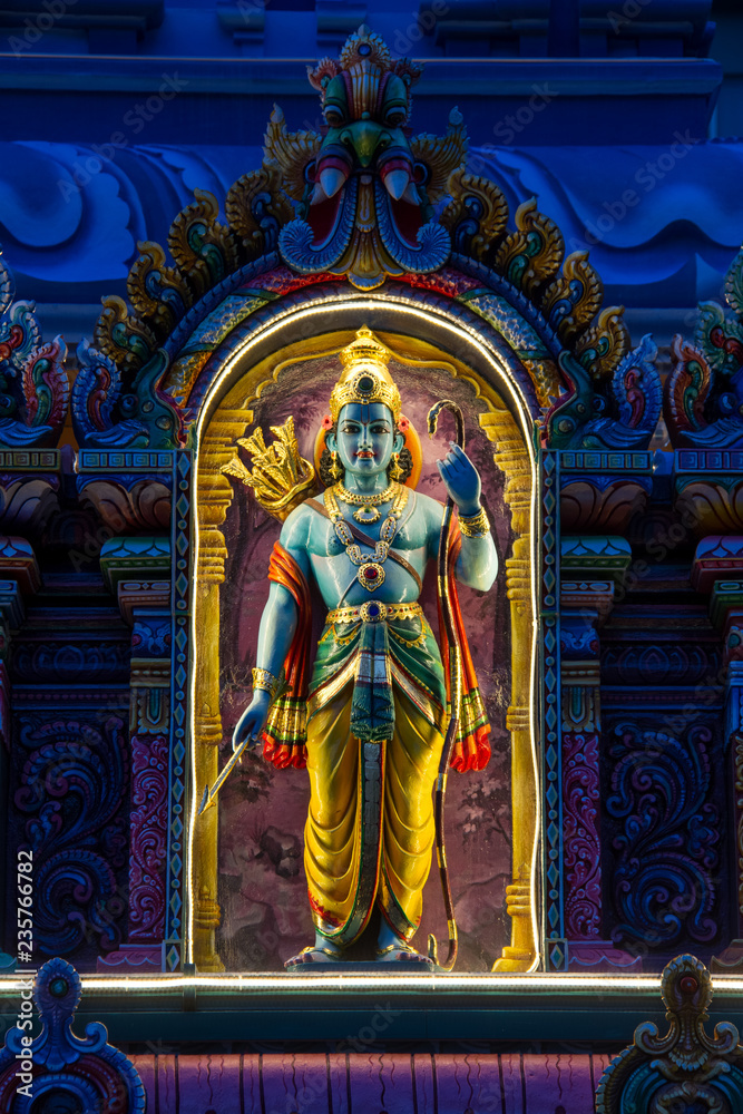 A nighttime image of an Indian deity lite up while standing in an arch.