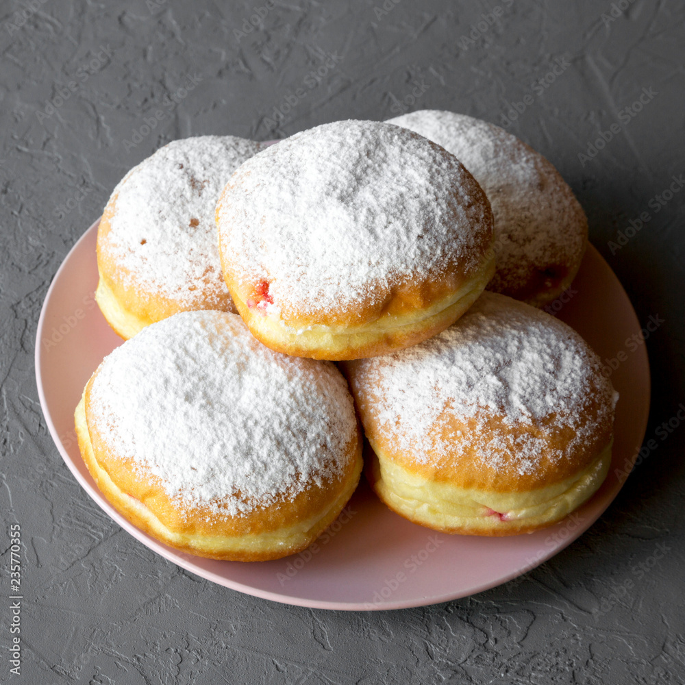 Homemade sweet donuts with powdered sugar on pink plate over grey background, side view. Closeup.