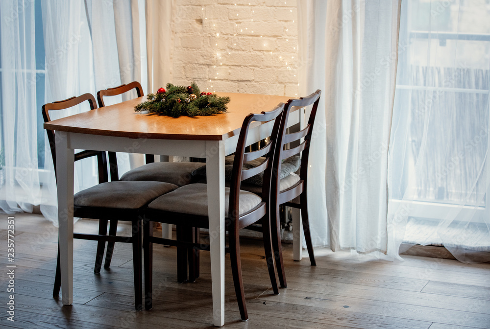 View on a Christmas tree branch decoration on table with chairs on a kitchen. View on a Christmas tree branch decoration on table with chairs on a kitchen.