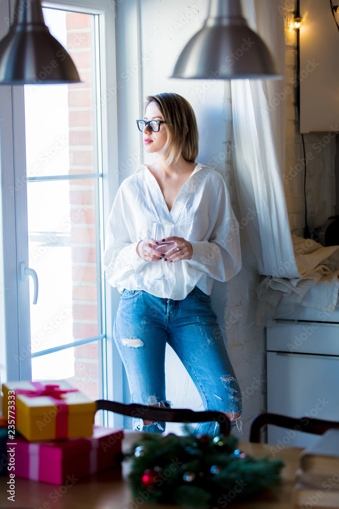 Young caucasian woman in white shirt and blue jeans with glass of a wine stay in a kitchen. Young caucasian woman in white shirt and blue jeans with glass of a wine stay in a kitchen.