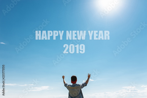 The man in the background, the blue sky, stretches his arms toward the sky. Text Happy New Year, on clouds, christmas concept.