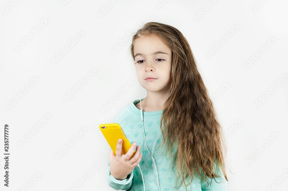 Bright beautiful little girl in headphones with the phone emotionally posing for a selfie on an isolated background. Bright beautiful little girl in headphones with the phone emotionally posing for a selfie on an isolated background.