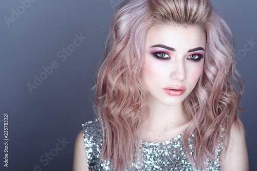 Close up portrait of beautiful young model with colorful artistic make up and wavy hairstyle wearing silver sequin top. Isolated on grey background. Text space