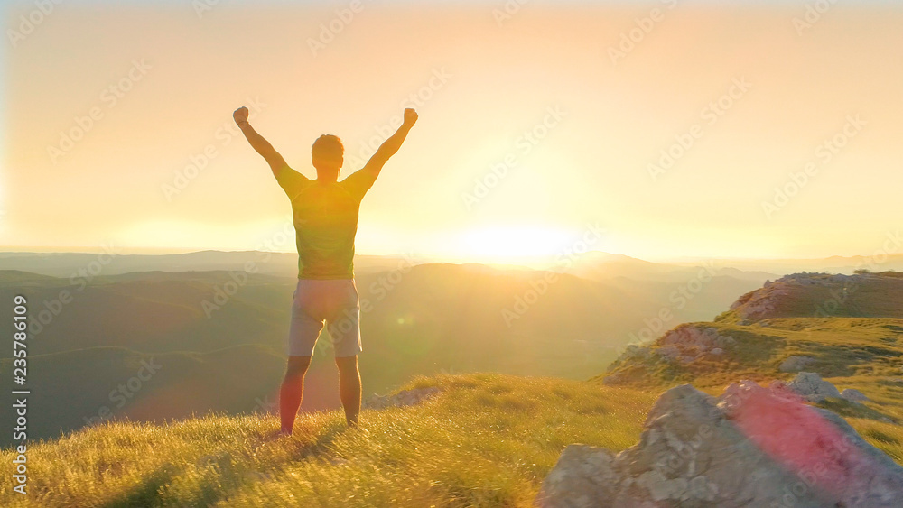 DRONE, LENS FLARE: Bright evening sun rays shine on the victorious male hiker.