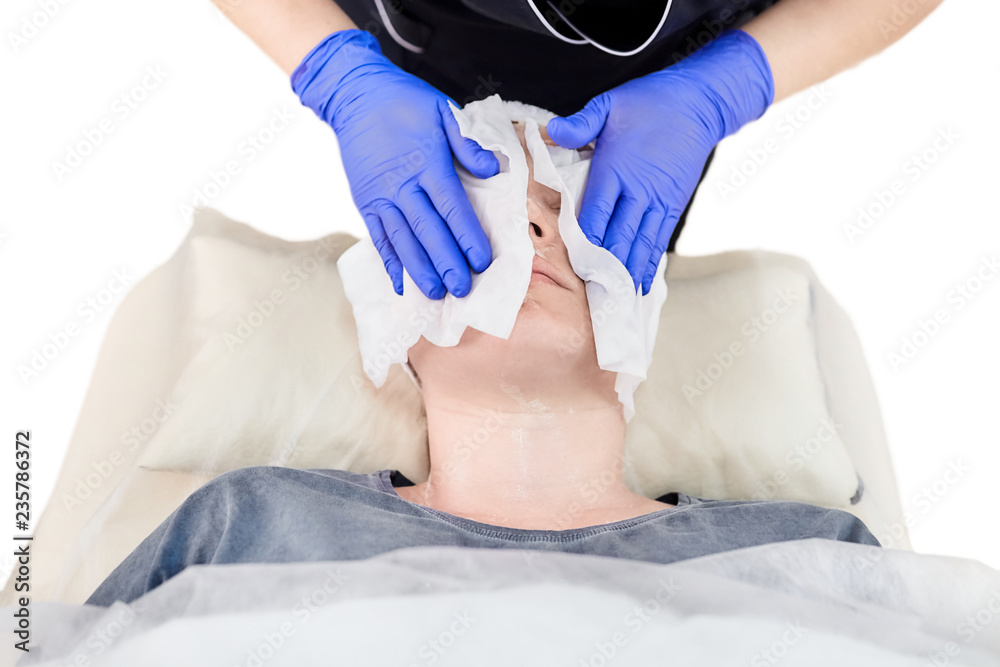 The process of removal a cosmetic cream from the face of a young woman. Hands of the cosmetologist in gloves. Facial skin care. Peeling The process of removal a cosmetic cream from the face of a young woman. Hands of the cosmetologist in gloves. Facial skin care. Peeling