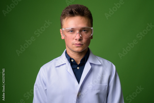 Young handsome man doctor wearing protective glasses against gre