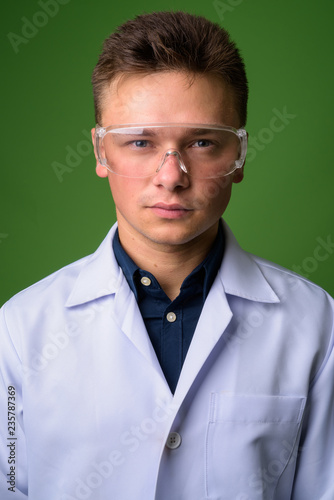 Young handsome man doctor wearing protective glasses against gre
