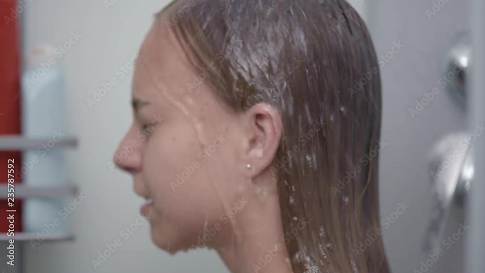 Young girl bathing under a shower at home - back view. Beautiful teen girl taking shower and washing in the bathroom. Happy child washing head, face and body with water. Stock ビデオ | Adobe Stock