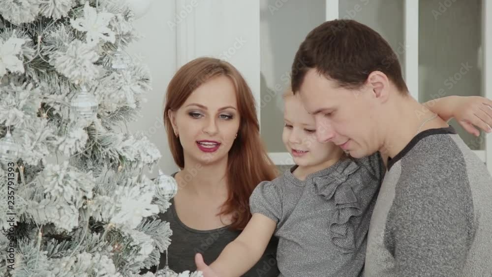 The family is standing near the Christmas tree, laughing talking and touching toys while waiting for Christmas. The family is standing near the Christmas tree, laughing talking and touching toys while waiting for Christmas.
