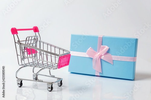 Small supermarket grocery push cart for shopping toy with blue gift box isolated on white background. Sale buy mall market shop consumer concept. Copy space