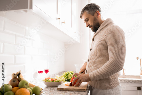 Side view portrait of bearded mature man cooking dinner in kitchen lit by sunlight, copy space