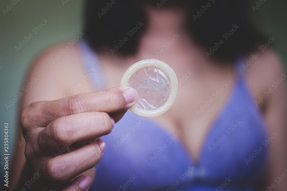 Woman showing a condom on bed, Focus on the condom in the foreground Woman showing a condom on bed, Focus on the condom in the foreground