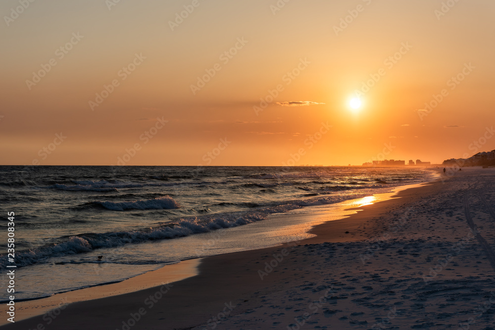 Orange yellow sunset in Santa Rosa Beach, Florida with Pensacola coastline coast cityscape skyline in panhandle with ocean gulf mexico waves, silhouette of buildings