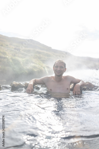 Young happy man swimming bathing in Hveragerdi Hot Springs on trail in Reykjadalur, during autumn summer morning day in south Iceland, golden circle, rocks, vertical view