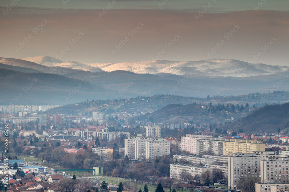 Winter cityscape of Eastern European communist era tower blocks in Miskolc city outskirts with forested hills and sunlit snow-capped Bukk Mountains in North Hungarian Mountain Range, Hungary Europe