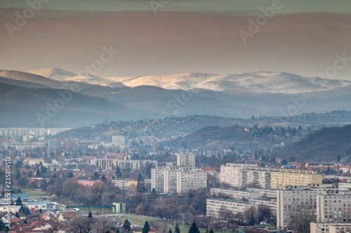 Winter cityscape of Eastern European communist era tower blocks in Miskolc city outskirts with forested hills and sunlit snow-capped Bukk Mountains in North Hungarian Mountain Range, Hungary Europe