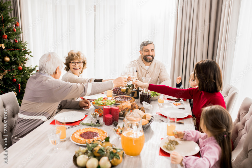Warm-toned portrait of big happy family enjoying Christmas dinner together and toasting