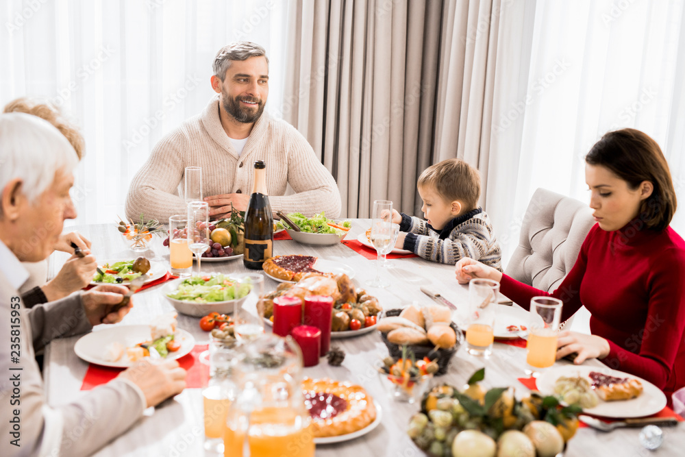 Warm-toned portrait of big happy family enjoying Christmas dinner together, focus on smiling man in head of table Warm-toned portrait of big happy family enjoying Christmas dinner together, focus on smiling man in head of table