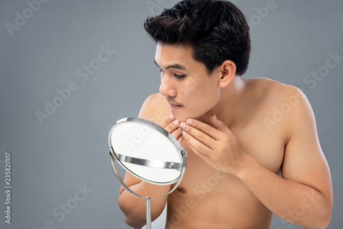 Young asian male model checking his face in mirror