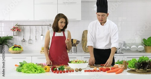 Asian chef demonstrate how to cut tomatoes pieces for beautiful woman in cooking class in white clean modern kitchen.