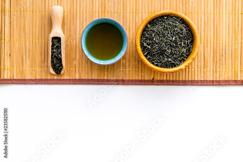 Chinese tea concept. Tea ceremony. Dry tea leaves in bowl and wooden scoop near cup of tea on white background and bamboo table mat top view copy space © 9dreamstudio