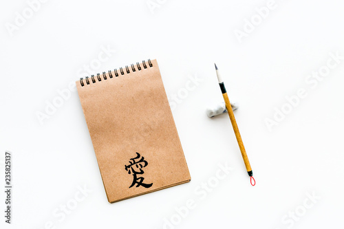 Chinese traditional calligraphy concept. Asian hieroglyph love in craft paper notebook near special writting pen on white background top view copy space