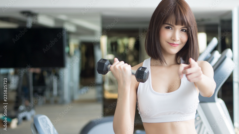 healthy strong fitness woman looking and pointing at you. portrait of fitness woman in gym posing for gym workout, looking and pointing to invite you to join the club. asian adult fitness woman model