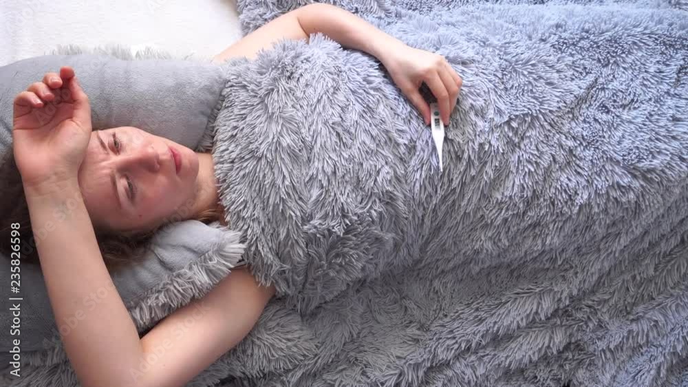 tired woman, measures the temperature with electronic thermometer. girl lies on the bed under a warm blanket, tired woman, measures the temperature with electronic thermometer. girl lies on the bed under a warm blanket,