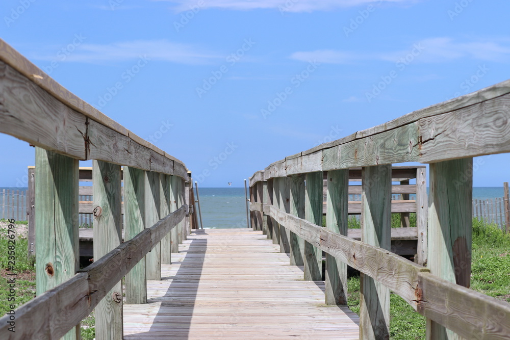 Perspective photograph of wood boardwalk railing beach access horizon blue sky, turquoise ocean and green grass. Perspective photograph of wood boardwalk railing beach access horizon blue sky, turquoise ocean and green grass.