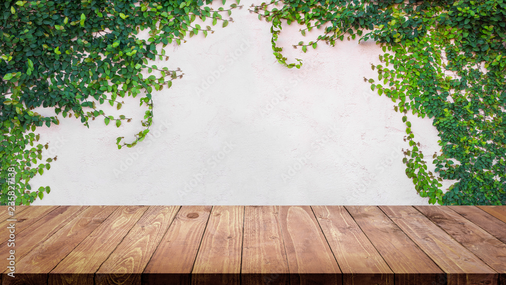 Empty wood table with ivy leaves on cement wall background.