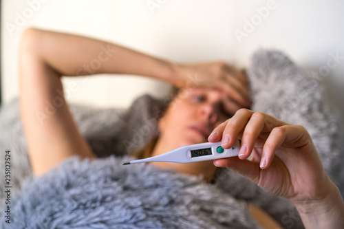 tired woman girl is lying on the bed under a warm blanket. Shows thermometer. close up.