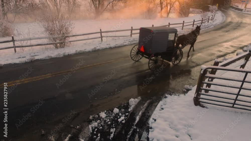 A horse-drawn Amish buggy travels through the snow-covered Pennsylvania countryside toward the Hunsecker's Mill Covered Bridge at sunset. Concept: winter, holidays, tradition, nostalgia, ?cold, snow