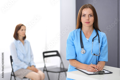 Doctor woman at work. Portrait of female physician filling up medical form while standing near reception desk at clinic or emergency hospital. Medicine and healthcare concept photo