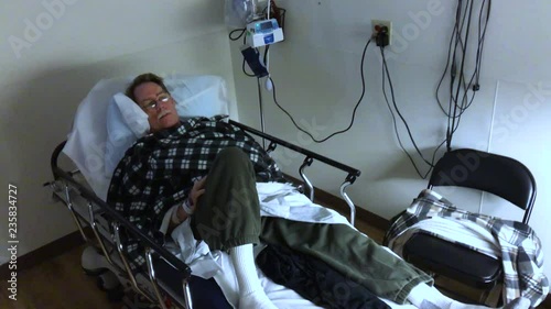 Sick middle aged man laying in ER hospital room, looking dazed and ill. Footage shot like walking up to him.