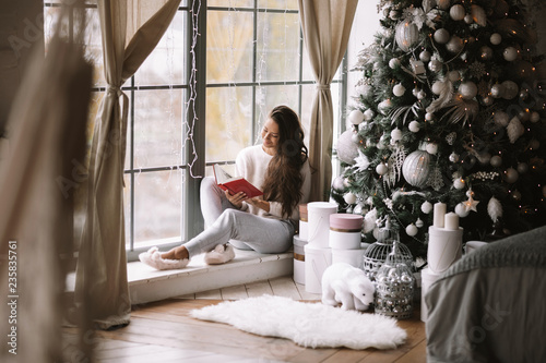 Cuadro en lienzo Nice dark-haired girl dressed in pants, sweater and warm slippers reads a book s