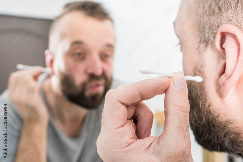 Obraz premium Man removing wax from ear using Q-tip
