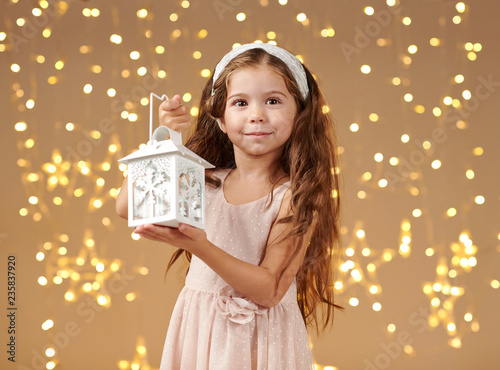 girl child is posing with lantern in christmas lights, yellow background, pink dress