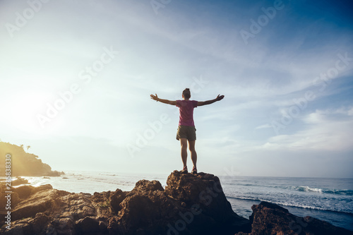 Freedom woman outstretched arms on sunrise seaside rock cliff edge