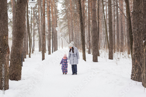Winter, childhood and people concept - mother is walking with her little daughter in snowy forest © satura_
