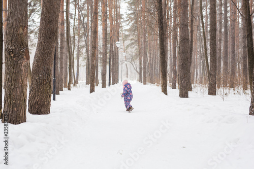 Child running in snowy forest. Toddler kid playing outdoors. Kid play in snowy park.