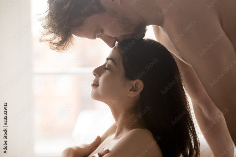 Passionate boyfriend kiss pretty girlfriend head during tender foreplay before love making in bedroom, young couple enjoying prelude before sex, man caressing woman, romantic moment at home close up Stock Photo 