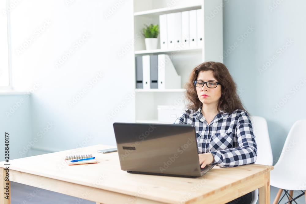 Technology, business and people concept - Serious woman in glasses working at the computer in office Technology, business and people concept - Serious woman in glasses working at the computer in office
