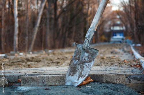 A shovel at a construction site stands against the background of a is paving walkway