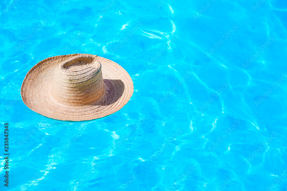 Straw hat on the surface of blue clear swimming pool with free space. Summer vacation concept.