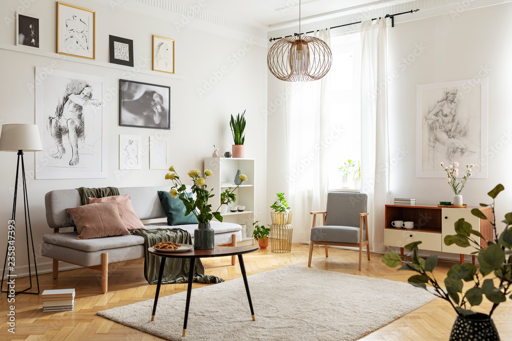 Table with flowers on carpet in apartment interior with posters above sofa  near armchair. Real photo Stock Photo | Adobe Stock