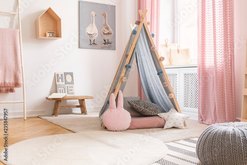 Pastel pillows in front of tent in girl's bedroom interior with pink drapes and poster. Real photo