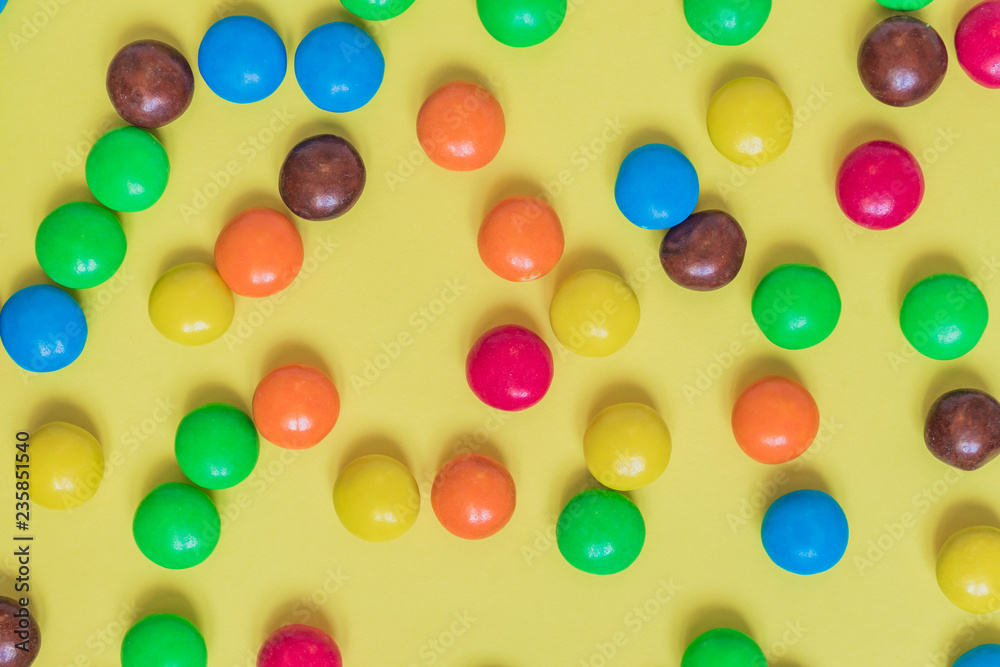 Colorful Background of multicolored sweet candies. Round bonbons scattered on yellow background