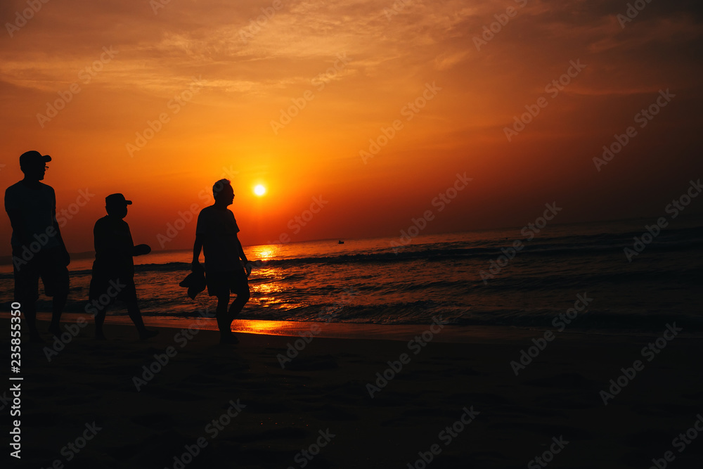 silhouettes of men on the beach by the sea on the background of orange sunrise and sky