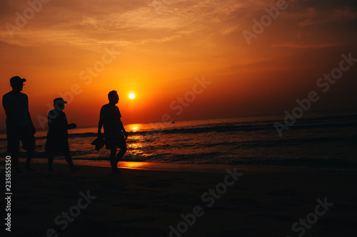 silhouettes of men on the beach by the sea on the background of orange sunrise and sky