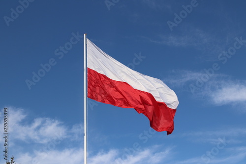 White-red horizontal flag on a flagpole developing in the wind against a blue sky with light clouds. Symbol of the Polish state.